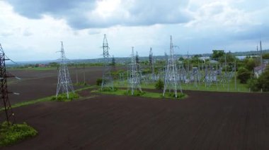 Yüksek elektrik iletim kuleleri bulutlu bir gökyüzünün altında geniş bir alana yerleştirilmiş ve enerji taşımacılığı ve dağıtımı için gerekli altyapıyı göstermektedir.