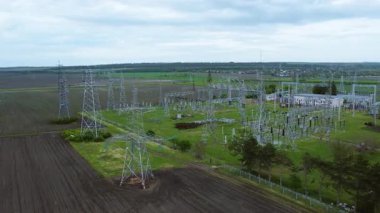 Yüksek elektrik iletim kuleleri bulutlu bir gökyüzünün altında geniş yeşil bir alana yerleştirilmiş ve enerji taşımacılığı ve dağıtımı için gerekli altyapıyı göstermektedir.