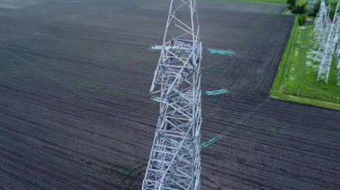 Yüksek elektrik iletim kulesi geniş tarım arazisinin üzerine yükseliyor, enerji altyapısı ve kırsal manzaranın karışımını vurguluyor, güç dağılımının önemini vurguluyor