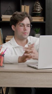 Üniversite öğrencisi rahat kütüphanede dizüstü bilgisayarda özenle çalışır. İnsan, kitaplar ve doğal ışık ile çevrili olarak oturur ve verimli bir atmosfer yaratır.