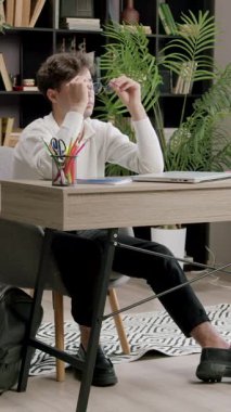 Genç adam masadan bardakları alır ve aksesuar takar. Çalışma alanı parlak ve düzenli bir şekilde çalışmaya devam ederken adam yerinde oturuyor.