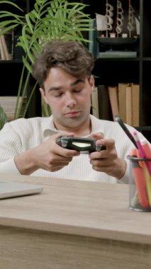 Genç adam heyecan verici bir şekilde masa başında bilgisayar ve eğitimi umursamadan joystick oynuyor. Adam oyalanma ve video oyunlarına bağımlılık gösteriyor.