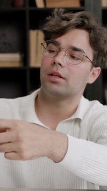 Gözlüklü kolej öğrencisi geziye gitmek için masa küresi seçiyor. Kütüphanede çalışan adam macera planlayan kitaplıklarla çevrili.