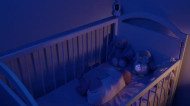 Bebek gece karyolasında monitör ve müzikal penguen lambasıyla uyuyor. Güvenlik kamerası ve rahatlatıcı oyuncak güvenli bir dinlenme sağlar.