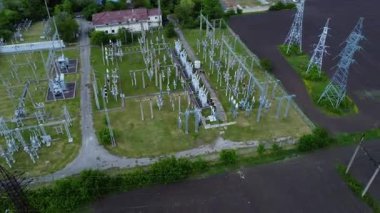 Elektrik hatları ve iletim kulelerinin yer aldığı, yeşil alanlar ve altyapı ile çevrili bir elektrik ağının hava perspektifi, enerji dağıtım sistemlerini gösteriyor