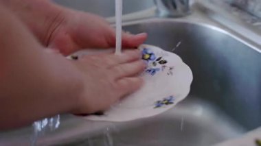 Eller, paslanmaz çelik bir lavaboda akan suyun altında beyaz bir bezi ovalıyor ve hastalıkların önlenmesi ve temizliği için etkili hijyen uygulamaları sergiliyor.