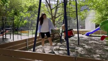 Neşeli bir çocuk parkında sallanıyor, çevrenin yeşillik ve renkli oyun ekipmanlarıyla çevrili, aile eğlencesi ve sevgi dolu anıların özünü yakalıyor.