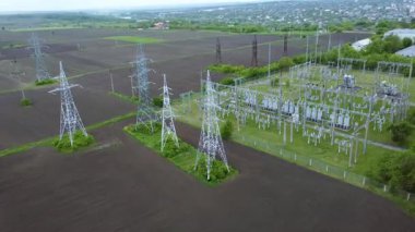 Yüksek voltajlı iletim kuleleri ve santralleri, yeşil alanlarla çevrili kırsal bir alanda enerji dağılımı ve bağlantılılığını gösteren bir ulusal elektrik ağı oluşturur.