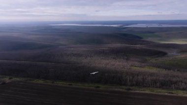 Bir planör uçağı engin yeşil alanlar ve yoğun ormanlar üzerinde zarif bir şekilde uçar, hava keşiflerinin özünü ve doğanın güzelliğini yakalar.
