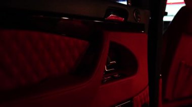 Zengin kırmızı döşeme ve şık metalik detaylara sahip lüks bir araç, çağdaş bir ortamda sofistike tasarım ve işçiliği vurguluyor