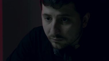 Kulaklıklı bir erkek, karanlık bir ortamda çalışıyor, nazik kırmızı ışıkla vurgulanıyor, gece verimliliğinin ruhunu yakalıyor.