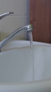 Çağdaş musluk, temiz beyaz bir lavaboya su dağıtır ve şık bir banyo ortamında sorumlu tüketim ve verimli su kullanımını vurgular.