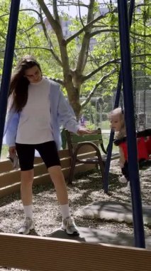 Neşeli bir çocuk parkında sallanıyor, çevrenin yeşillik ve renkli oyun ekipmanlarıyla çevrili, aile eğlencesi ve sevgi dolu anıların özünü yakalıyor.