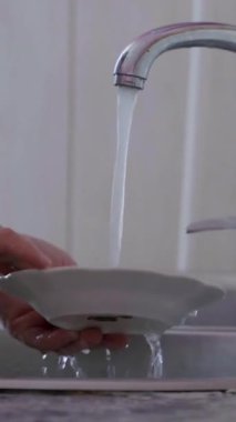 Enfeksiyon önlemedeki temizliğin önemini vurgulamak için temiz bir mutfak lavabosunda akan su ve düzenli bir tezgahla bulaşıkları yıkıyor.