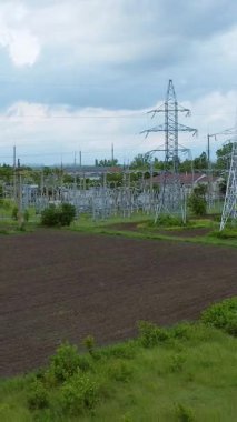 Elektrik ağı, açık alan ve dramatik bulutlarla çevrili yemyeşil bir alanda enerji altyapısını gösteren yüksek iletim hatlarına sahiptir.