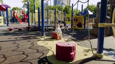 Canlı oyun alanı tırmanma yapıları ve slaytlarıyla dolu, renkli oyun alanları ve düşen yapraklarla çevrili, ekipmanla meşgul olan bir çocuğu gösteriyor.