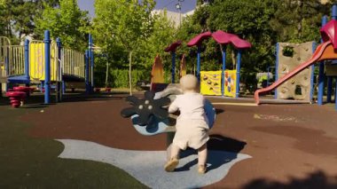 Bebek, canlı oyun alanı özellikleriyle etkileşime giriyor, güvenli bir açık havada güneşli bir günün tadını çıkarıyor, oyun yoluyla fiziksel aktiviteleri ve sosyal becerileri teşvik ediyor.