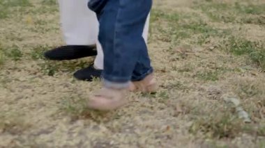 Bebek güvenli bir şekilde ilk adımlarını atıyor. Yetişkinlerin destekleyici varlığıyla yeni başlangıçların heyecanını ve hareketin neşesini vurguluyor.