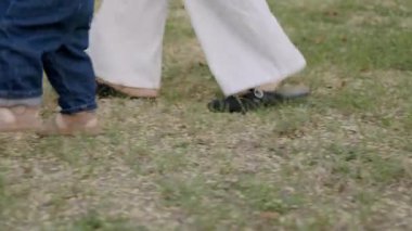 Bebek, bir yetişkinin elini tutarak yürümeye çalışıyor. Çimlerin üzerinde kararsız adımlar atıyor. Erken hareketliliğin ve keşiflerin heyecanını gösteriyor.