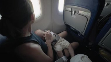 Anne, uçak koltuğunda uyuyan bebek beşiği, seyahat sırasında sevgi ve konforun özünü yakalıyor, huzurlu ortamı ve yakın ilişkiyi vurguluyor.