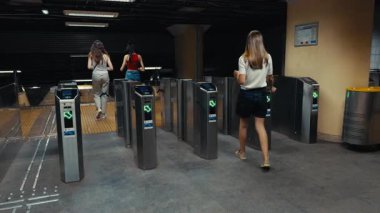 Dişi gezgin metro turnikelerinde kartını tarıyor, girişten geçiyor, şehir içi ulaşımın ve modern ulaşım deneyiminin dinamik akışını yakalıyor.