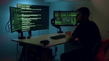 Erkek girişimci, karanlık bir odada kod ve analizlerle dolu çift taraflı bilgisayar monitörleriyle, dijital yenilik ve konsantrasyon atmosferini vurguluyor.