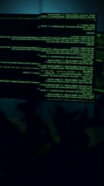 Deneyimli yazılım geliştirici, karmaşık programlama metni ve verileriyle dolu parıldayan ekranlarla çevrili loş bir ortamda kodlamaya odaklanmış durumda.