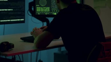 Erkek programcı, canlı ortam aydınlatması ve çoklu monitörlerle çevrili, parlak bir masada kodlamaya odaklanmış, dinamik bir çalışma alanı atmosferi yaratıyor.