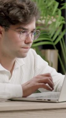 Erkek tipler dizüstü bilgisayarda odaklanmış ifade ve sabit eller ile rapor verirler. Sahne, canlı bitkiler ve parlak çalışma alanı araçlarına sahip kitaplıkları içerir