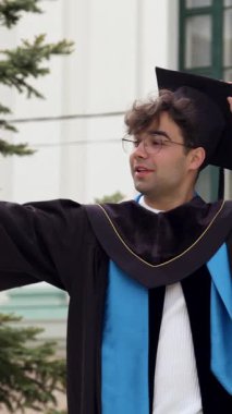 Happy Mezun 'un elinde geleneksel havan panosunu ayarlayan bir video kaydı var. Önlüklü öğrenci, üniversite binasının yanında köknar ağacıyla duruyor.