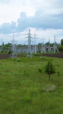 Elektrik iletim kuleleri, bulutlu bir gökyüzü ile çevrili yemyeşil bir alanda, enerji taşımacılığının temel altyapısını gözler önüne seriyor.