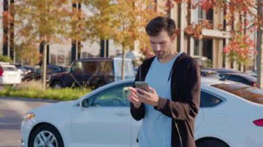 Erkek bireyler şehirde kiralık aracın kilidini açmak için mobil uygulama ile etkileşime girerken, çağdaş mimari ve canlı düşüş yaprakları dinamik bir kentsel sahne oluşturur.