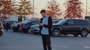 Erkek şahıs, işlek şehir otoparkındaki kiralık araca erişmek için mobil uygulama ile etkileşim halinde, yenilikler ve kentsel hareketliliğin kolaylığı vurgulanıyor