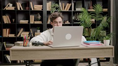 Modern bir ofiste internetli bir dizüstü bilgisayarın önünde çalışan genç bir serbest çalışan. Bilgisayarda daktilo eden ve müşterilerle uzaktan çalışan gözlüklü yakışıklı bir adam.