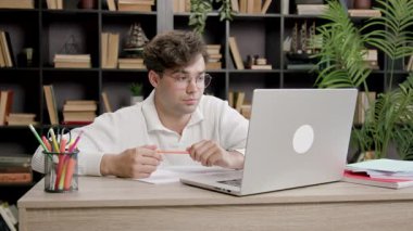 Genç çocuk bir bilgisayar ekranına bakıyor ve ihtiyatlı bir şekilde gülümsüyor. Yakışıklı çocuk derslere katılıyor ve laptoptaki bilgileri dikkatle dinliyor.