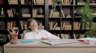 Öğrenci çalışmaya ara verir ve gözlerini ve ellerini dinlendirir. Modern bir kütüphanede yorgun bir çocuk ekstra çalışır ve bir dizüstü bilgisayarın önünde derslere hazırlanır ve notlar alır.