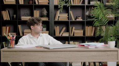 Öğrenci çalışmak ve sınavlara ve sınavlara hazırlanmak için havasında değil. Ofis masasında oturan gözlüklü çocuk üniversiteye başlamak istemiyor. Öğrenci derslerden sıkıldı