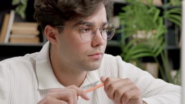 Masada düşünceli ve gülümseyen bir öğrenci, online derslere katılıyor. Genç adam, aklına bir fikir geldiğini ve not defterine not aldığını göstererek başını sallar. Modern bir kütüphanede öğrenci