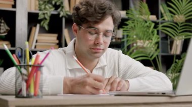 Yakışıklı otantik bir öğrencinin portresi şık bir ofiste, evde dizüstü bilgisayar kullanarak ders çalışıyor ve notlar alıyor. Çocuk teknolojilerin yardımıyla internete girip internetten öğrenim görüyor.