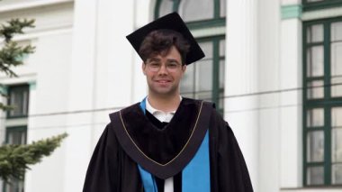 Siyah bornoz ve kafasında şapkayla mezuniyet töreninde gururla kameraya bakarak gülümsüyor. Mezun olduğu en iyi uluslararası üniversitenin avlusundaki genç çocuk.