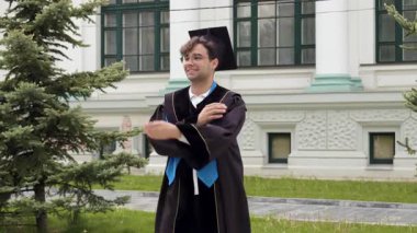 Gururlu mezun öğrenci elleri göğsünde mezuniyet elbisesi ve şapkasıyla ayakta duruyor. Üniversiteden başarıyla mezun olan ve uluslararası yüksek öğrenim diploması alan mutlu çocuk.