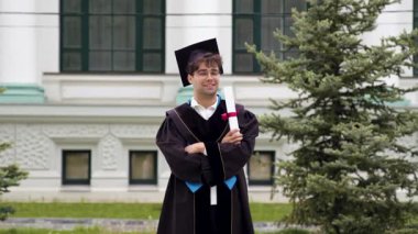 Siyah bornoz giymiş ve başında şapkası olan mezun bir çocuk elleri kollarının altında uluslararası bir üniversiteden mezuniyet diplomasını gururla tutuyor. Başarılı mutlu öğrenci.