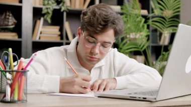 Genç uzman online ileri eğitim dersleri alıyor, dizüstü bilgisayardaki hoparlörleri dinliyor ve not defterine not alıyor. Çocuk, çevrimiçi kurslar ve konferanslar sayesinde kariyerinde büyüyor.