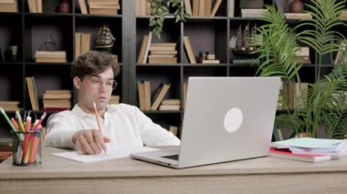 Dizüstü bilgisayarın önünde sandalyede oturan serbest çalışan çocuk ekranda gördüklerinden memnun değil ve hayal kırıklığına uğruyor. Genç adam çalışmalarının sonuçlarına üzüldü. uzak görev