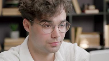 Gözlüklü, daktilo eden ve dokunmatik bir şekilde çalışan genç bir adamın yüzünü yakından çek. Çocuk uzaktan çalışıyor ve işinden zevk alıyor. Bu süreçten zevk alıyor.