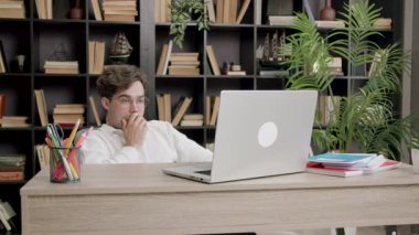 Çok yorgun genç çocuk esniyor ve çok çalışmaktan uykulu hissediyor. Gözlüklü öğrenci online üniversite seminerlerine katılıyor ve tartışmalara uzaktan yakından dahil oluyor