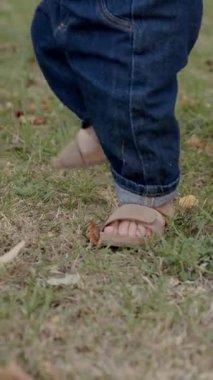 Bebek çimen ve yapraklarla meşgul, canlı bir açık havada dokuları ve renkleri keşfediyor, merakın ve duyusal keşfin özünü yakalıyor.