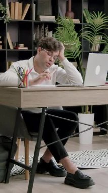 Modern bir ofiste çalışan yorgun ve yorgun genç bir uzman. Gözlüklü çocuk dizüstü bilgisayarın önünde saatlerce çalıştığı için çok çalıştı. İnternet teknolojileri ile iş ve çalışma.