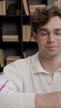 A boy student sitting on a bench in a classroom looks directly at the camera, smiles and demonstratively raises his hand up as a sign that he wants to answer,to give his opinion.Good manners at school