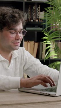 Kıvırcık saçlı ve görme bozukluğu olan genç bir öğrenci hafifçe gülümseyip bilgisayar başında çalışıyor. Samimi bir ofisteki dizüstü bilgisayarda tatmin olmuş çocuk tipleri ve uzaktan internetten öğrenim görüyor.